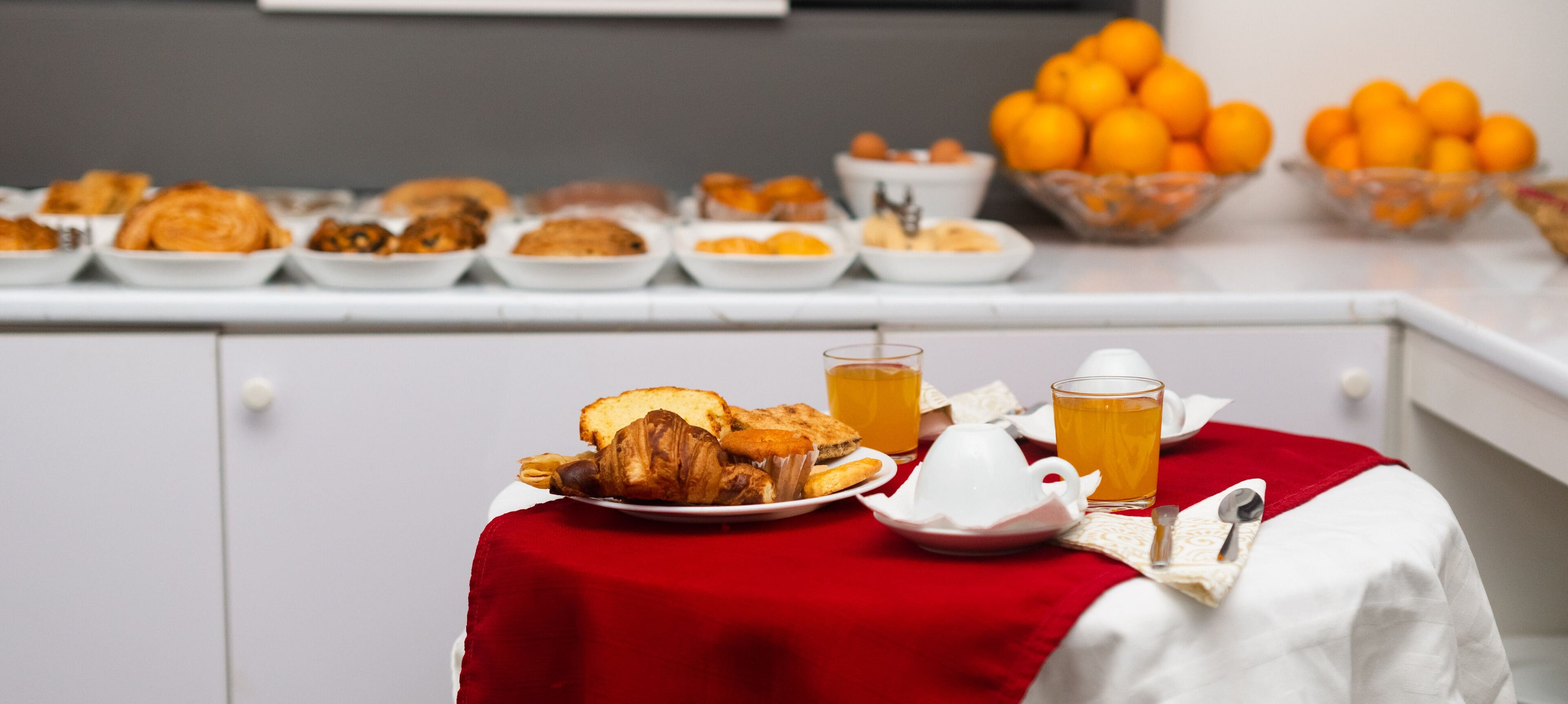 Una mesa de desayuno con croissants, tostadas y zumo de naranja.