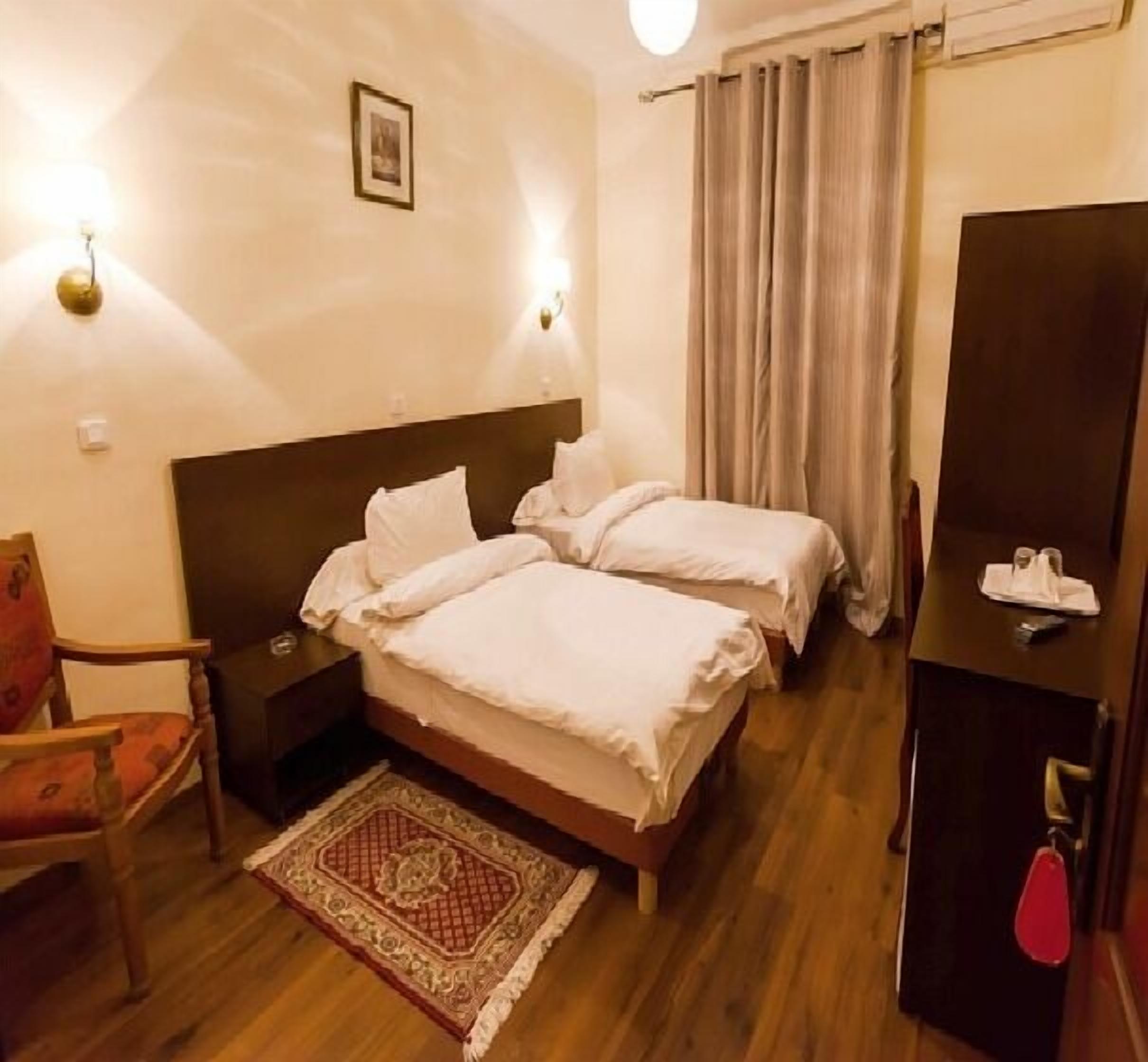 Una camera d'albergo con due letti, un comodino, una sedia, una scrivania e una lampada da tavolo.
