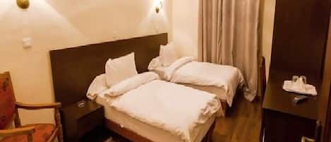 Una camera d'albergo con due letti, un comodino, una sedia, una scrivania e una lampada da tavolo.