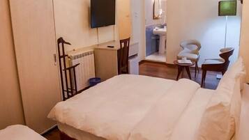 A hotel room with a bed, a television mounted on the wall, a bathroom with a sink and mirror, and a chair.