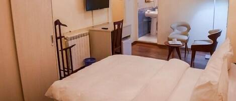 Una habitación de hotel con cama, televisor montado en la pared, baño con lavamanos y espejo, y una silla.