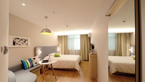Ett modernt hotellrum med en soffa, ett litet bord, ett skrivbord, två sängar, en spegel och ett fönster med gardiner.