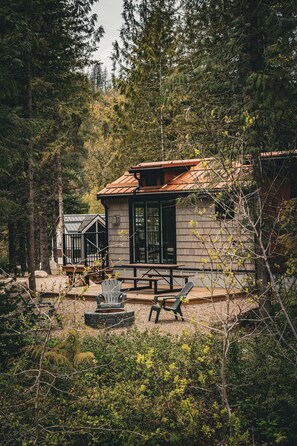 Una cabaña con terraza de madera, un brasero y mobiliario exterior.