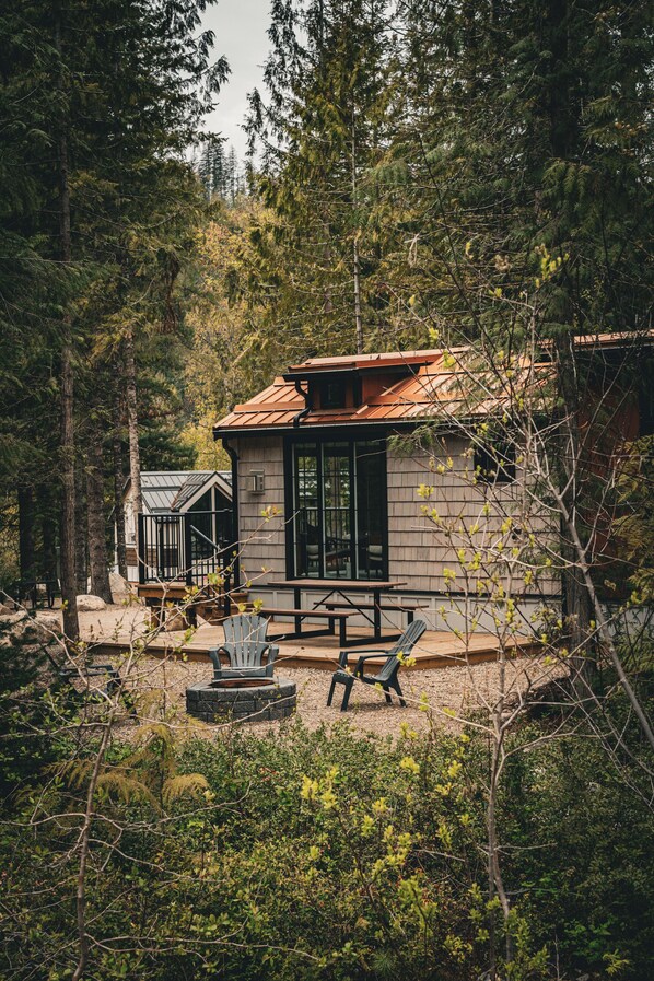 Una cabaña con terraza de madera, un brasero y mobiliario exterior.