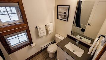 A bathroom with a window, a toilet, a sink, and a mirror.