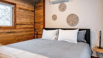 A bedroom with a wooden ceiling, a bed with grey bedding, a white air conditioner, and three wall-mounted clocks.