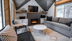 Un salon chaleureux avec une cheminée, un canapé, une table basse et un téléviseur posé sur une étagère en bois.