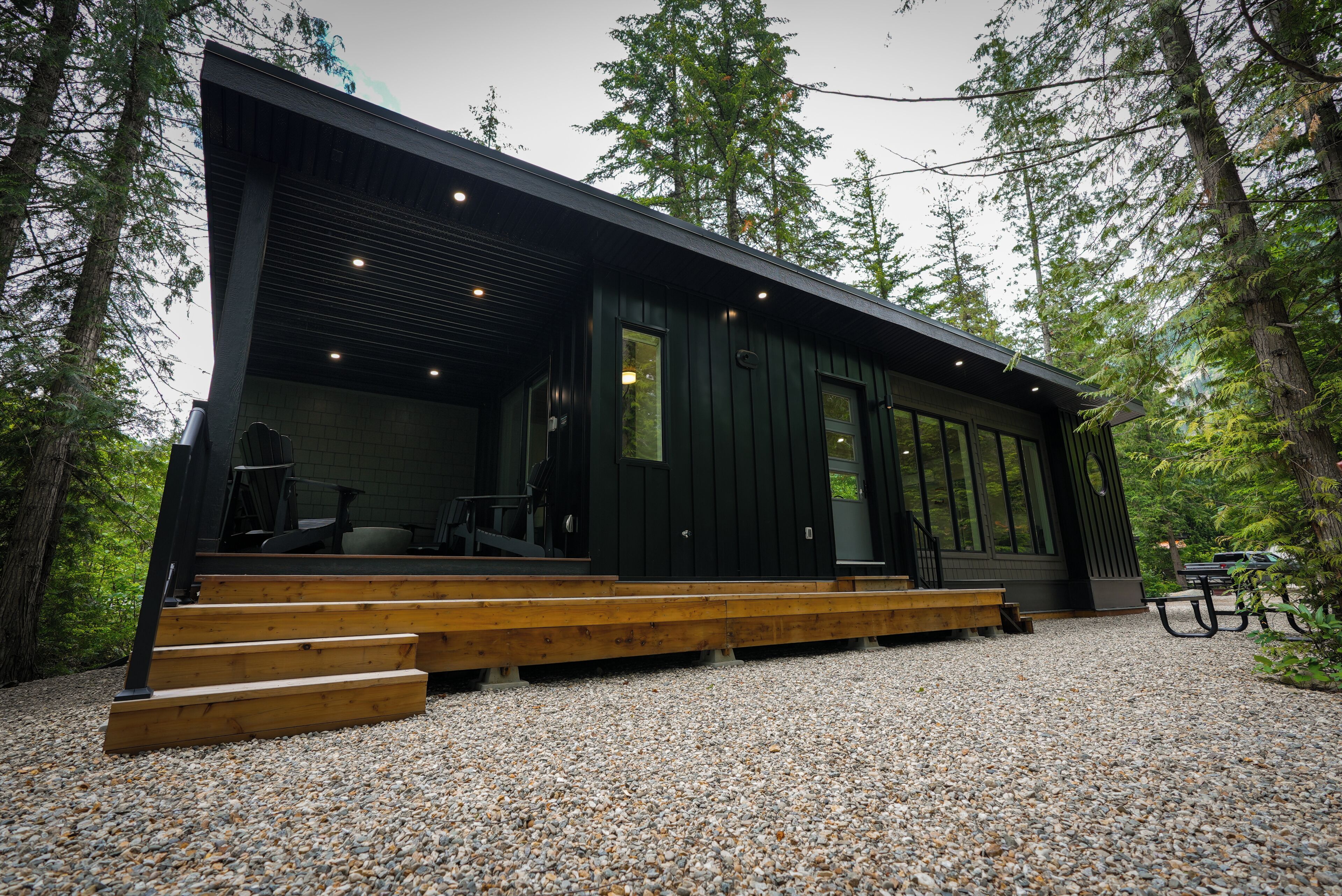 A modern cabin with a wooden deck and large windows, surrounded by trees.