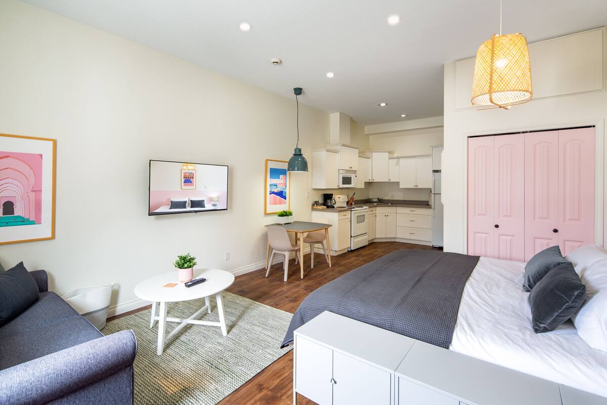 Habitación de hotel moderna con cama, sofá, mesa de comedor, área de cocina y televisor.