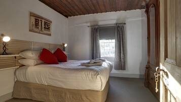 A bedroom with a large bed, a wooden ceiling, a window with curtains, and a picture on the wall.