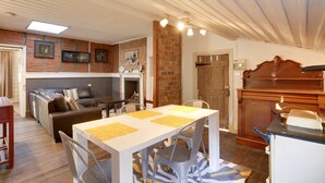 A dining area with a white table, grey chairs, and yellow placemats. There is a brick wall with framed pictures above the table. - White's Corner (Bothwell)