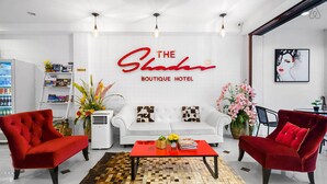 A hotel lobby with a white sofa, red armchairs, a red coffee table, and a wall sign reading "The Shaker Boutique Hotel". - The Shades Boutique Hotel Patong Phuket (Patong)