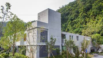 A modern building with a flat roof, surrounded by greenery and rocks.