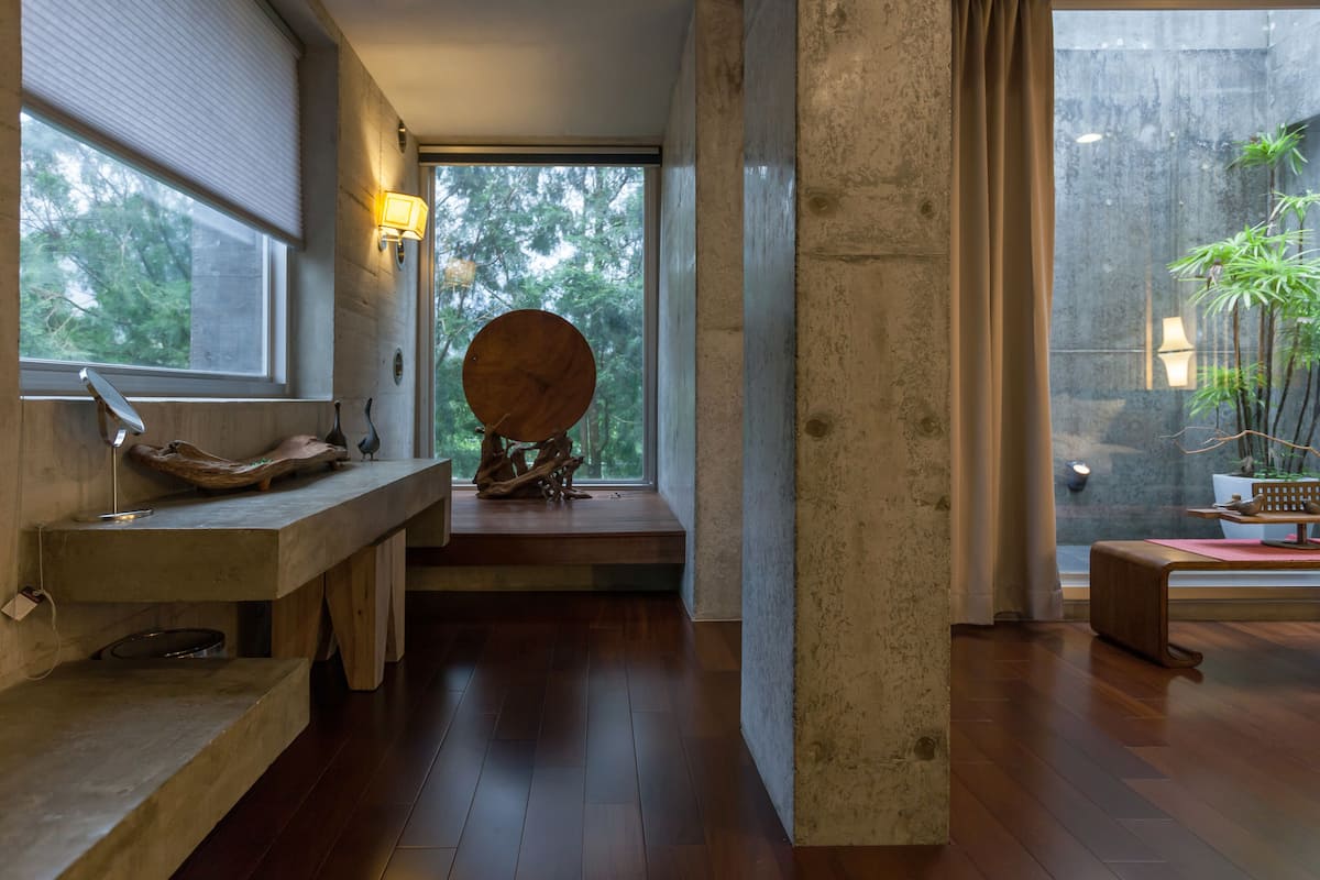 A modern interior with a wooden bench, a round wooden sculpture, and a view of greenery through large windows.