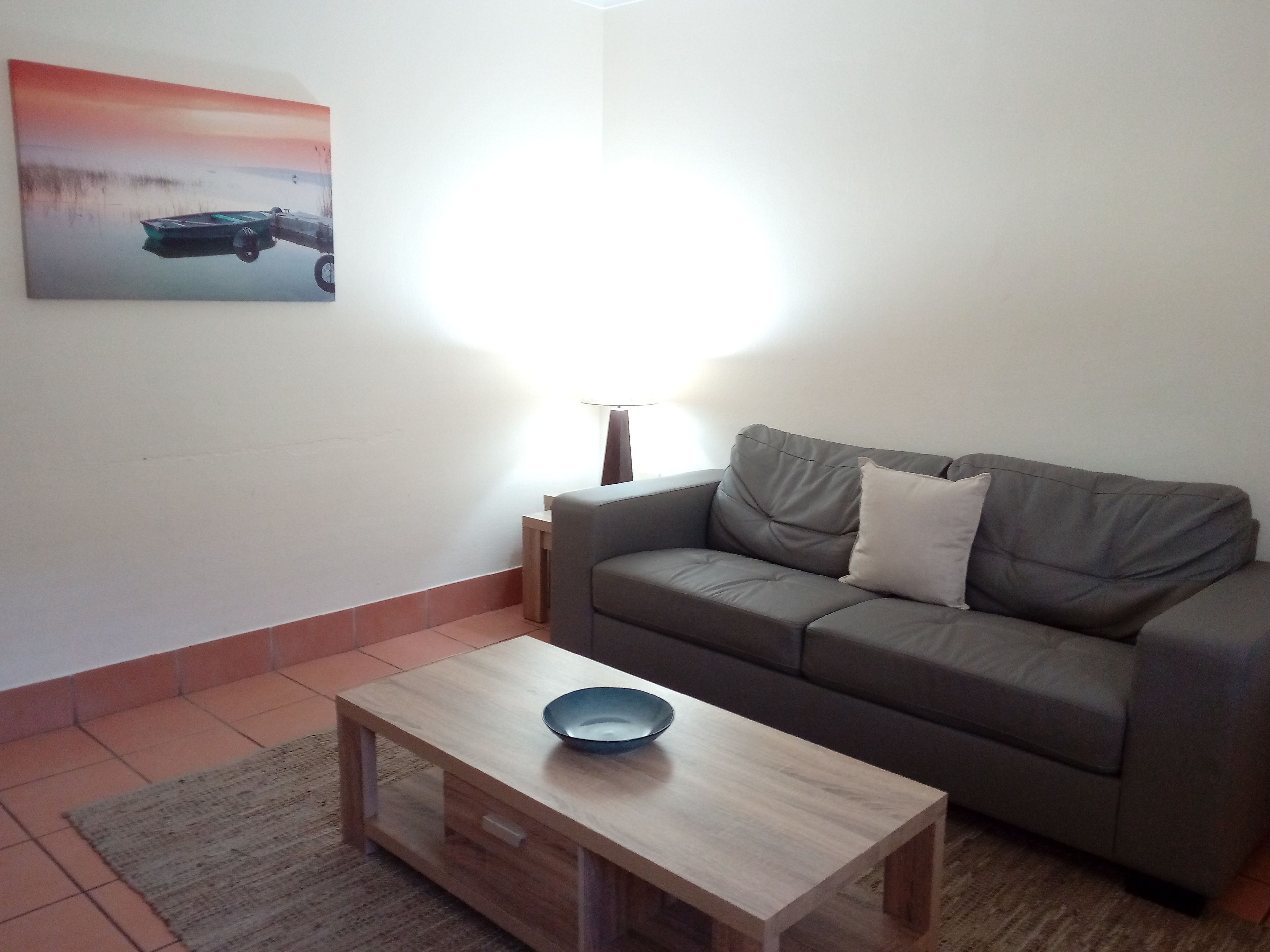 Een woonkamer met een bank, een bijzettafeltje, een lamp en een schilderij aan de muur.