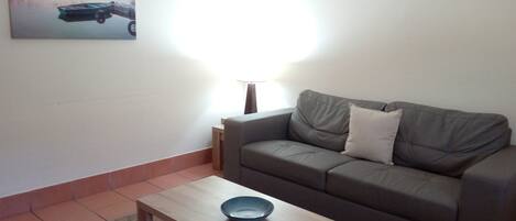 Een woonkamer met een bank, een bijzettafeltje, een lamp en een schilderij aan de muur.