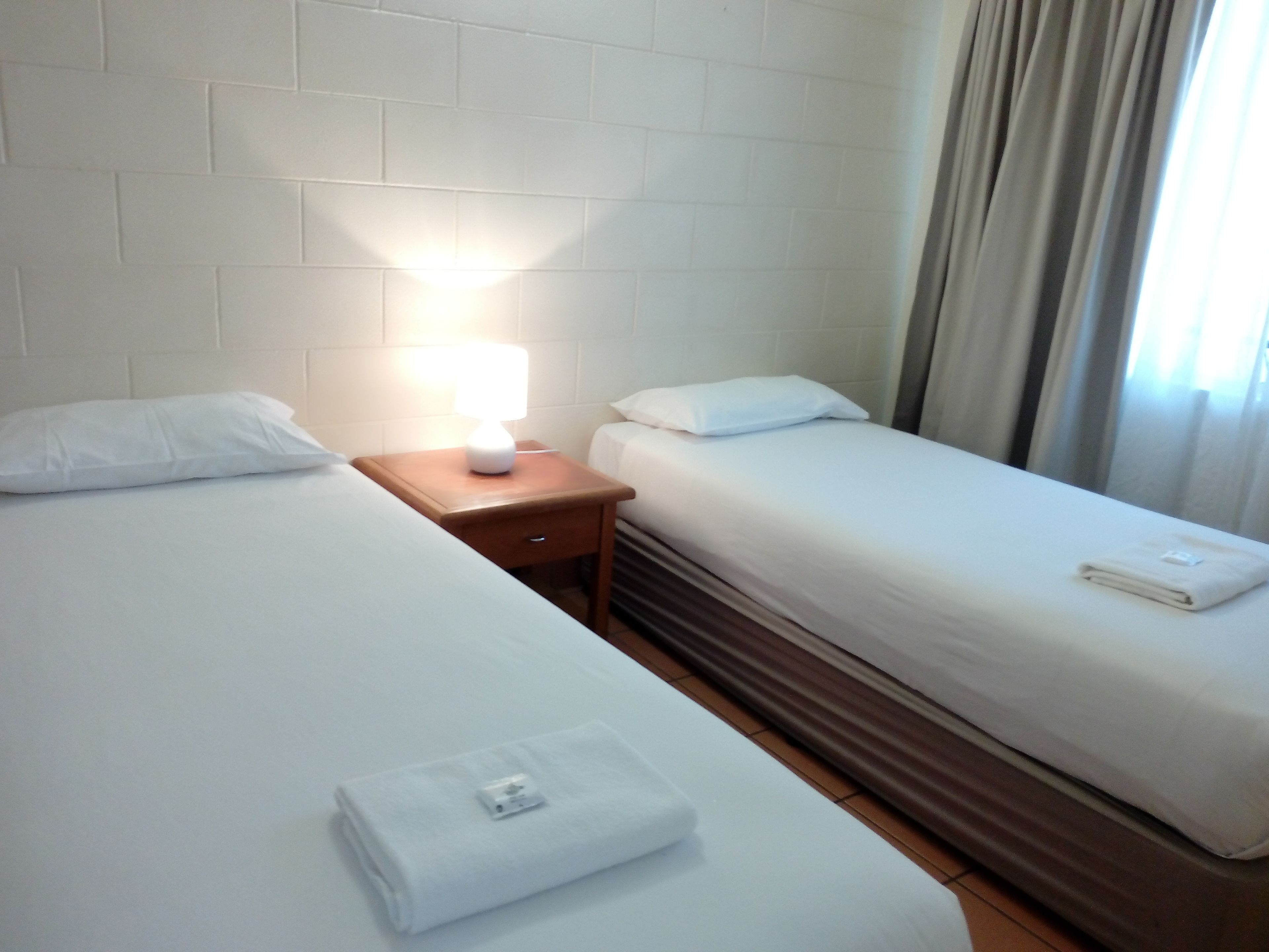Habitación de hotel con dos camas, una mesita de noche con lámpara y una toalla doblada en el suelo.