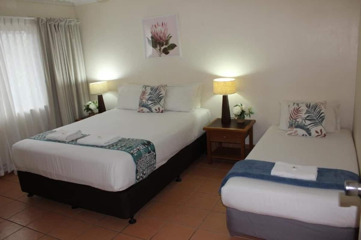A hotel room with two beds, each with a pillow and a bedside table with a lamp.