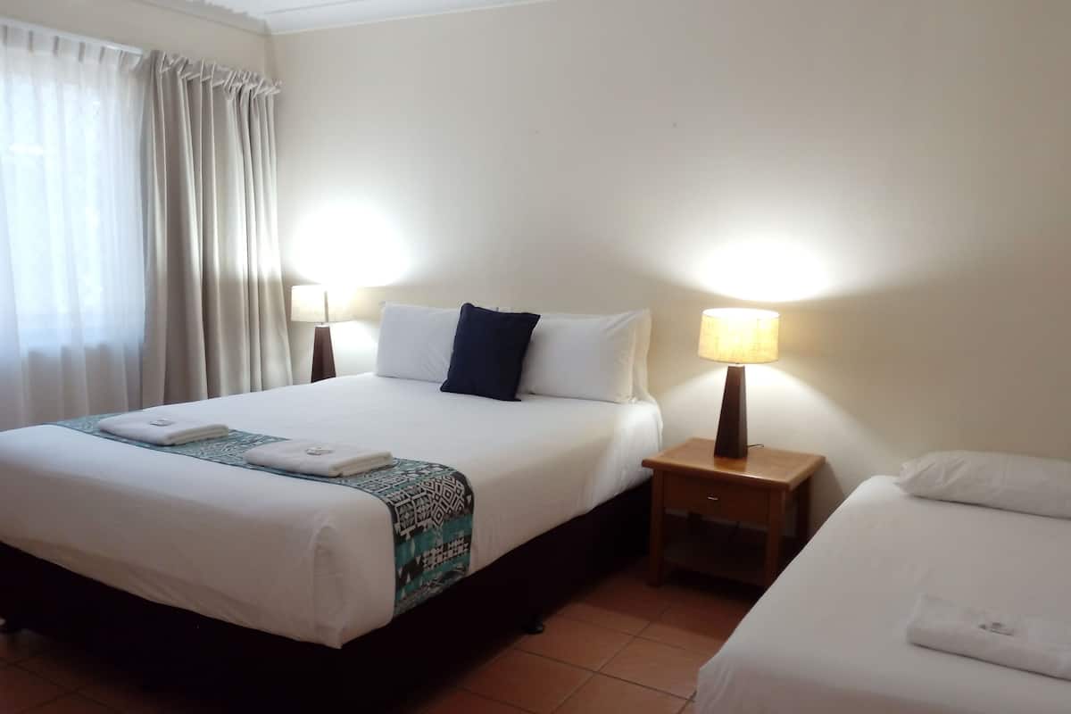A hotel room with a large bed, a smaller bed, two bedside tables with lamps, and a window with curtains.