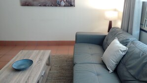 Una sala de estar con un sofá azul, una mesa de centro de madera y un cuadro que representa una playa.