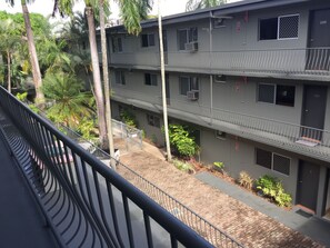 A multi-story building with balconies, air conditioning units, and a paved ground area with plants. - Lake Central (Cairns)