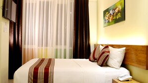 Una habitación de hotel con una cama, una mesita de noche con un teléfono, un cuadro en la pared y cortinas.