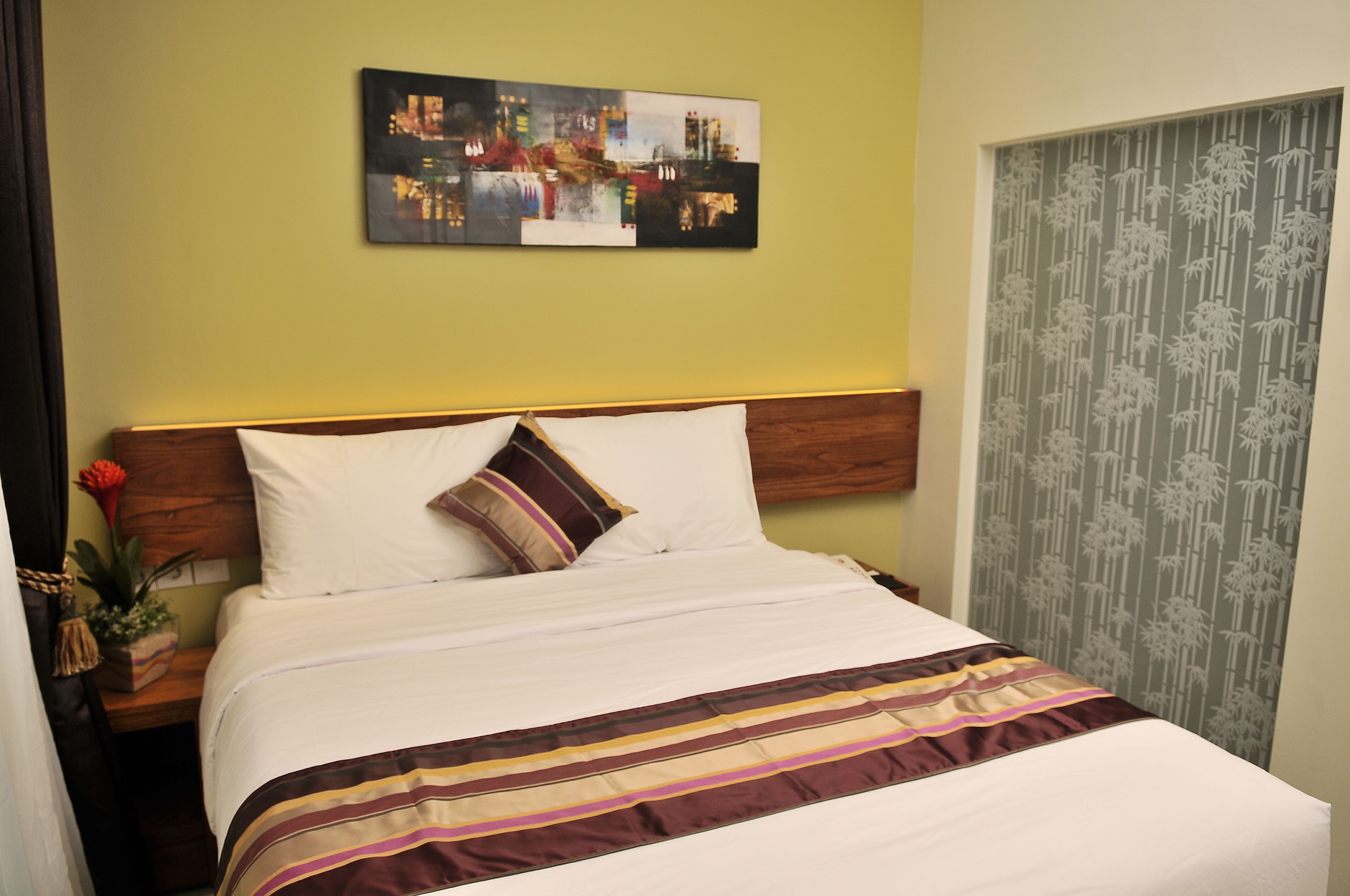 Una cama bien tendida con un edredón a rayas, una almohada y un cabecero frente a una pared verde.