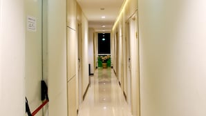 Un pasillo largo e iluminado con puertas a ambos lados, que conduce a una habitación con una planta verde y un objeto negro en el suelo.