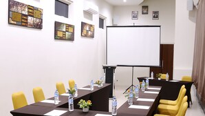 Un salón de conferencias con una larga mesa, sillas amarillas y una pantalla para proyector.