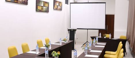 Un salón de conferencias con una larga mesa, sillas amarillas y una pantalla para proyector.