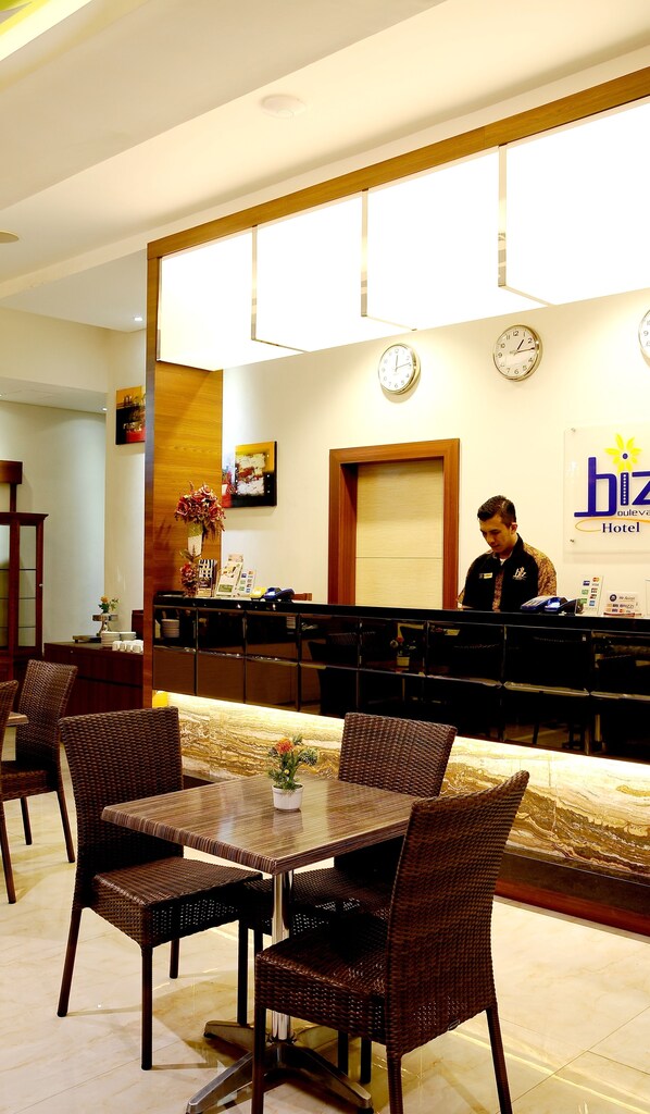 A hotel reception area with a receptionist, a reception desk, a clock, and a sign for the hotel. - Biz Boulevard Hotel (Manado)