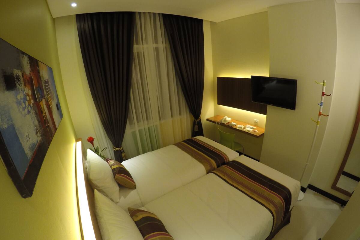 A hotel room with a bed, a desk with a telephone, a TV mounted on the wall, and a painting on the wall.