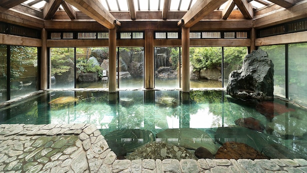 Una amplia piscina cubierta con agua cristalina, rodeada de paredes de piedra y vigas de madera.
