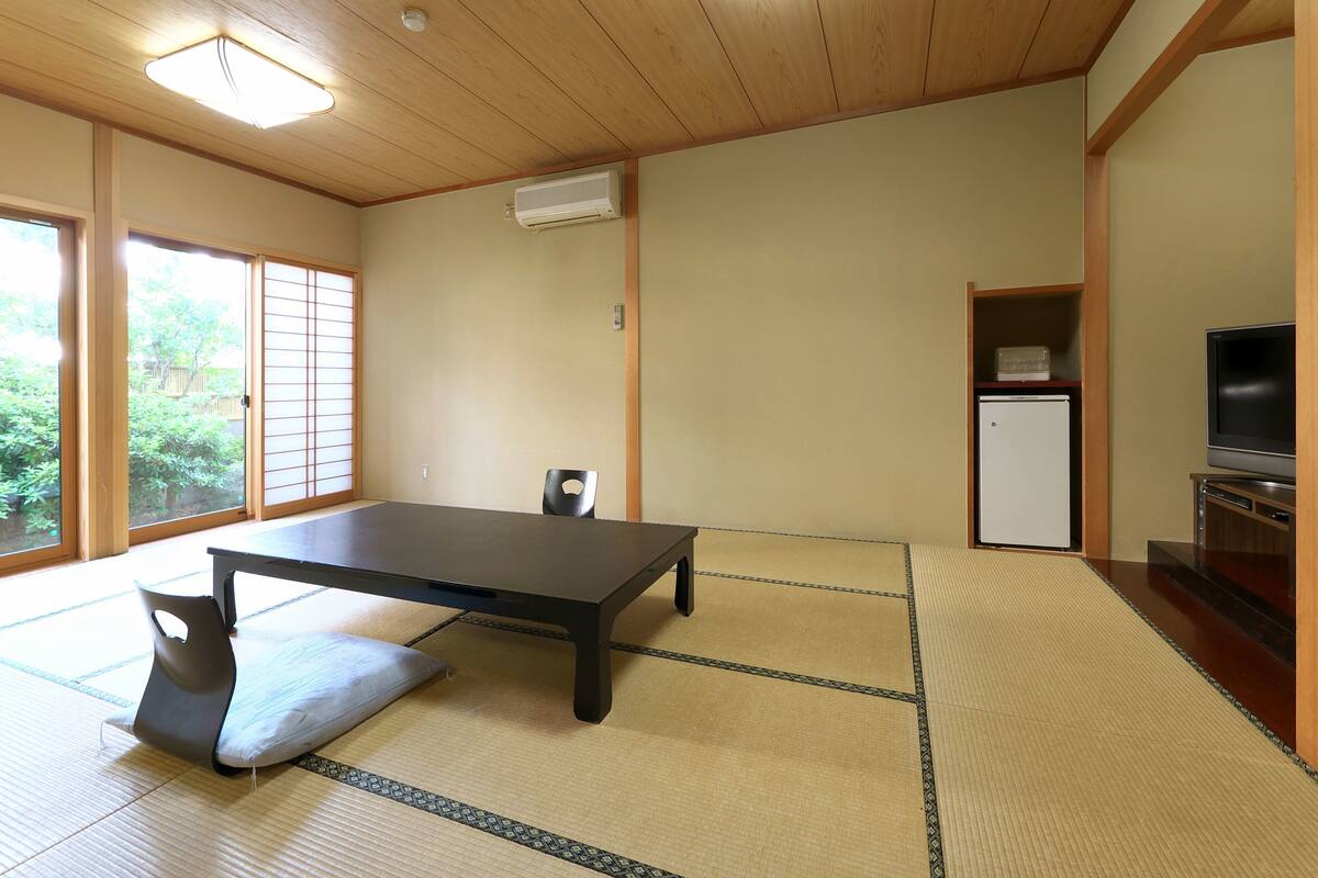 Una habitación de estilo japonés tradicional con suelo de tatami, una mesa baja, un cojín, un televisor y un refrigerador.