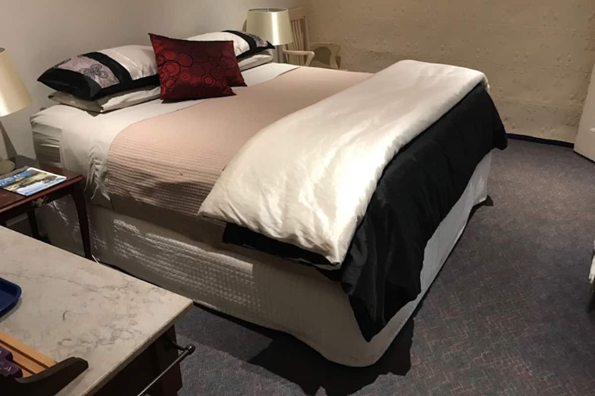 A hotel room with a bed, a bedside table, a lamp, and a chair.