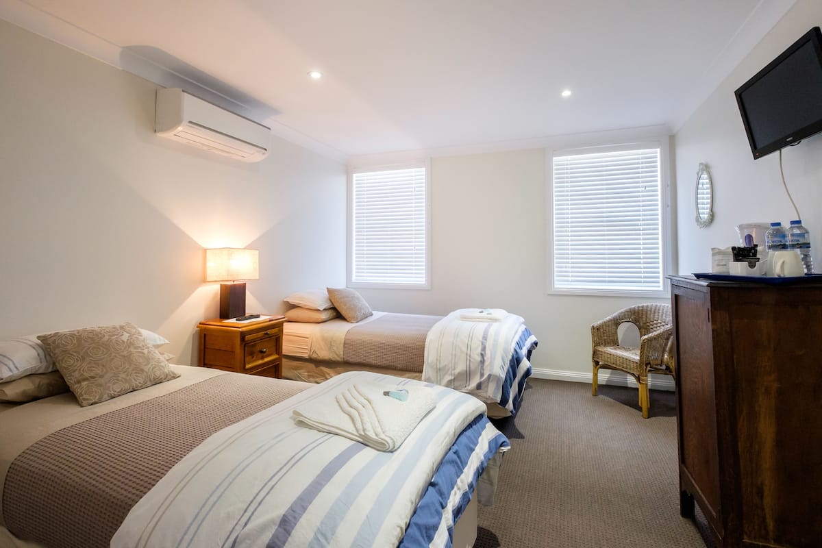 A hotel room with two beds, a desk, a chair, an air conditioner, and a TV on the wall.