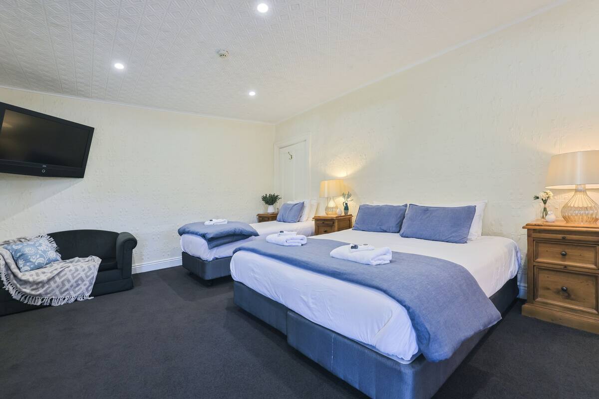 A hotel room with two beds, a flat-screen TV, a sofa, and a lamp.