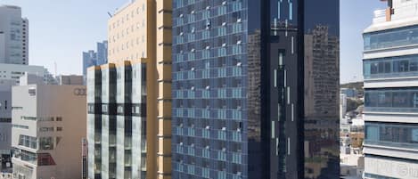 A modern hotel with a prominent glass facade, located in a busy urban area with other high-rise buildings.