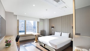 A modern hotel room with a large bed, a desk with a chair, a small table, and a window with a view of buildings. - Benikea Hotel Haeundae (Busan)