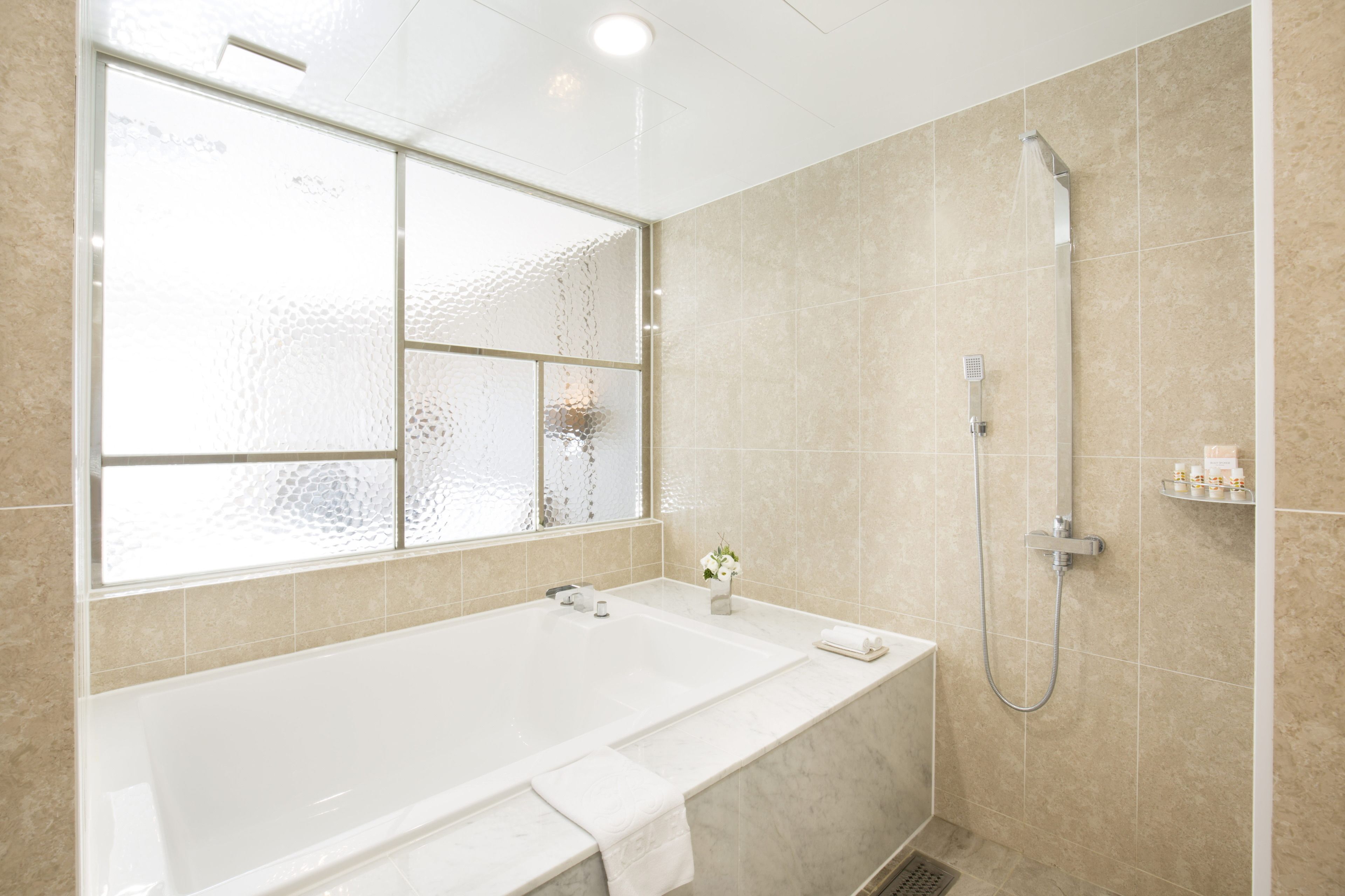 Et moderne badeværelse med et stort badekar, en brusekabine med glasvægge og et vindue med matteret glas.