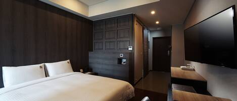 A modern hotel room with a large bed, a flat-screen TV, and a wooden desk.