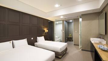 A hotel room with two beds, a desk with a mirror, and a bathroom visible through an open door.