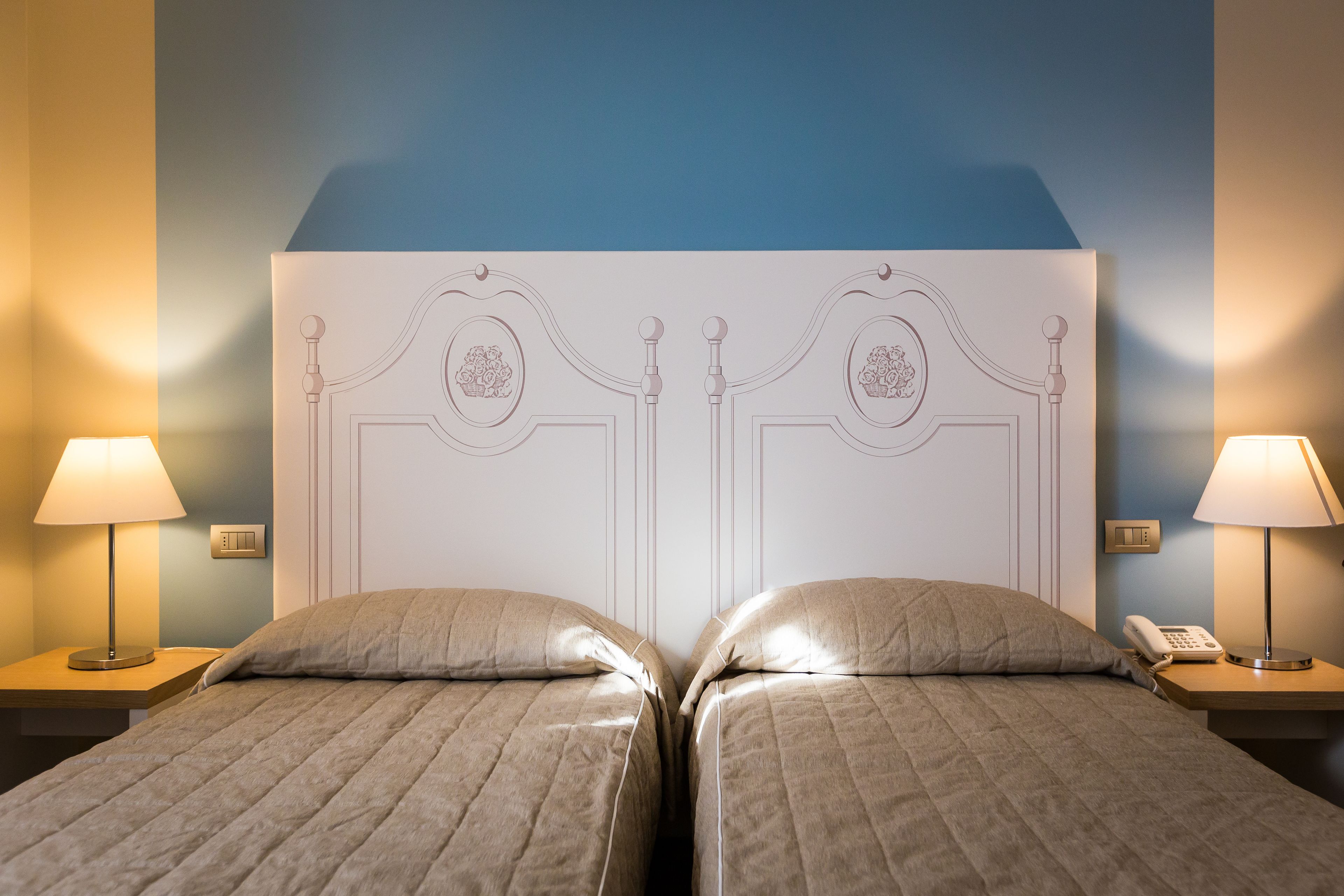 A hotel room with two beds, a headboard with decorative elements, bedside lamps, and a phone on the nightstand.