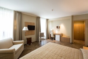 A hotel room with a bed, a desk, a chair, a TV, and a wardrobe.