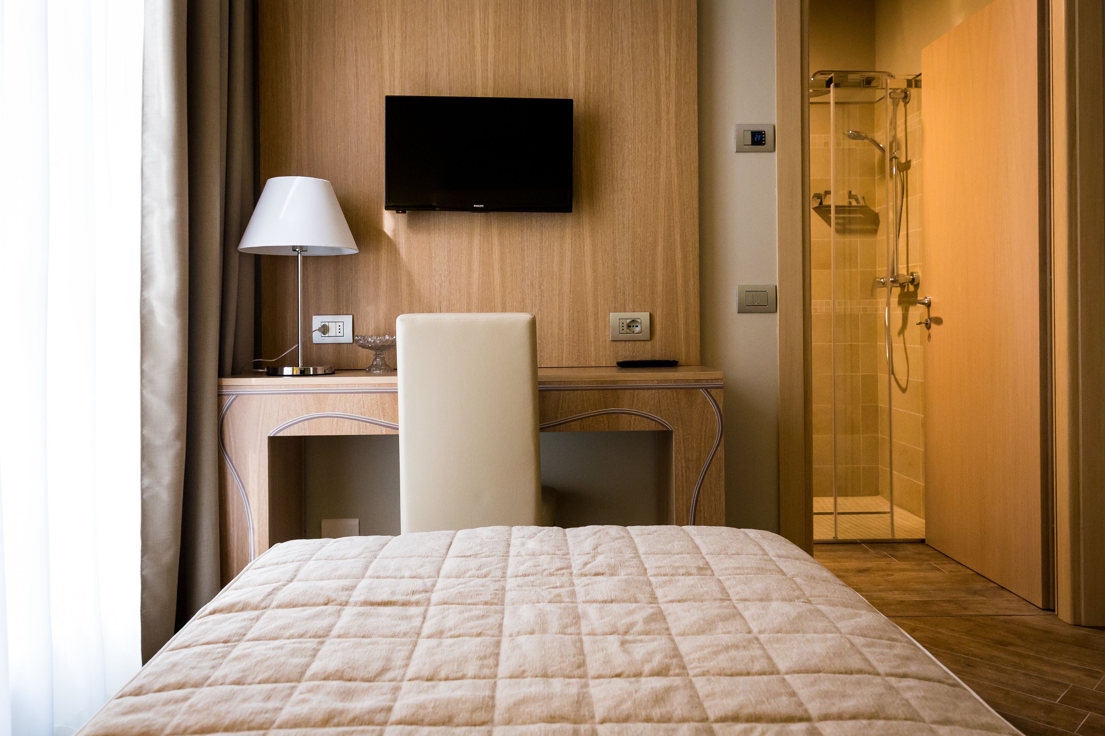 A hotel room with a bed, desk, chair, TV, and a shower area.