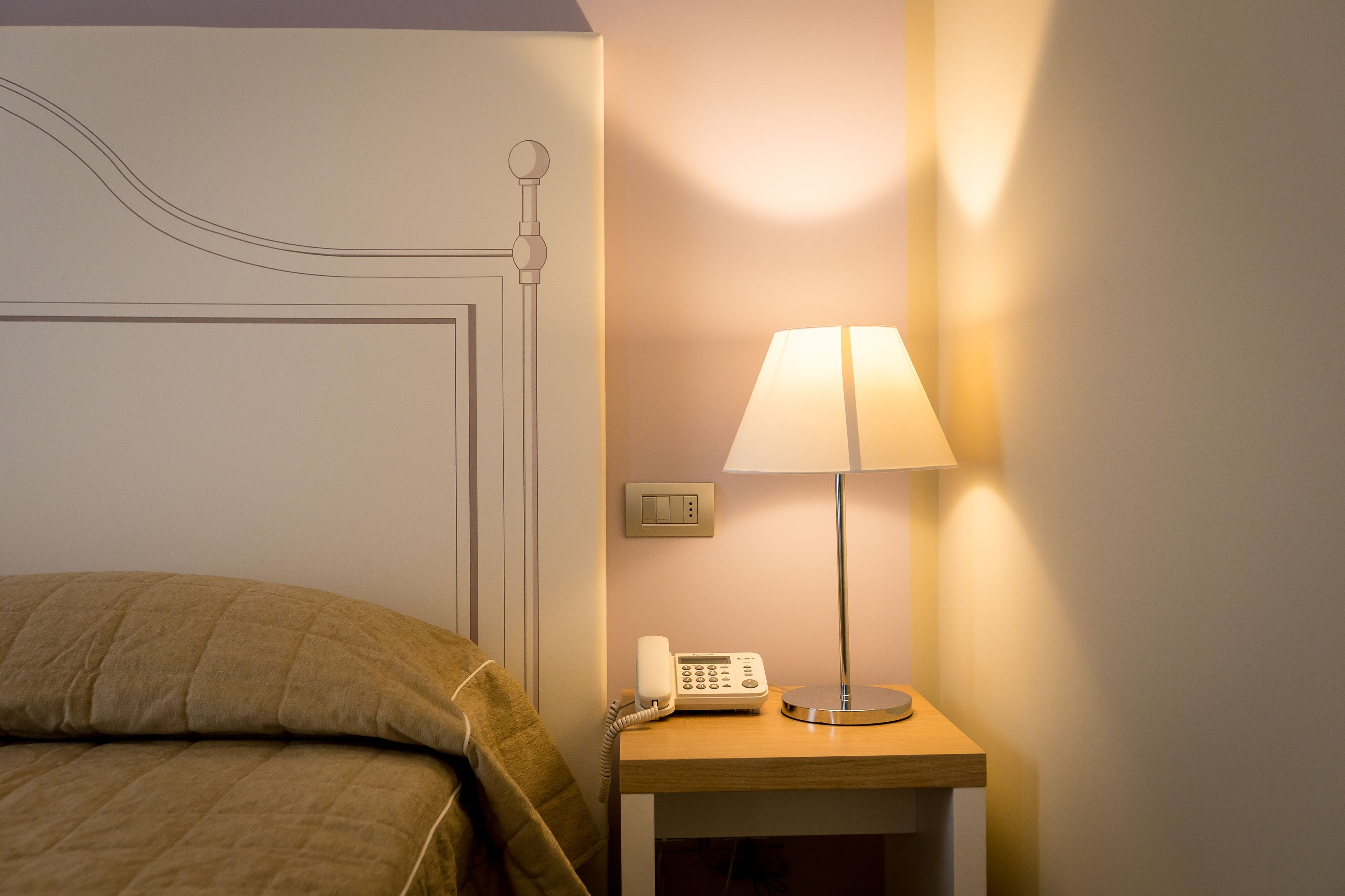 Et hotelværelse med en seng, et natbord med lampe og telefon.
