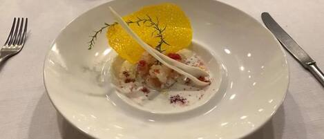 A white plate with a dessert featuring a yellow element, possibly a fruit or vegetable, and a white sauce with red specks.