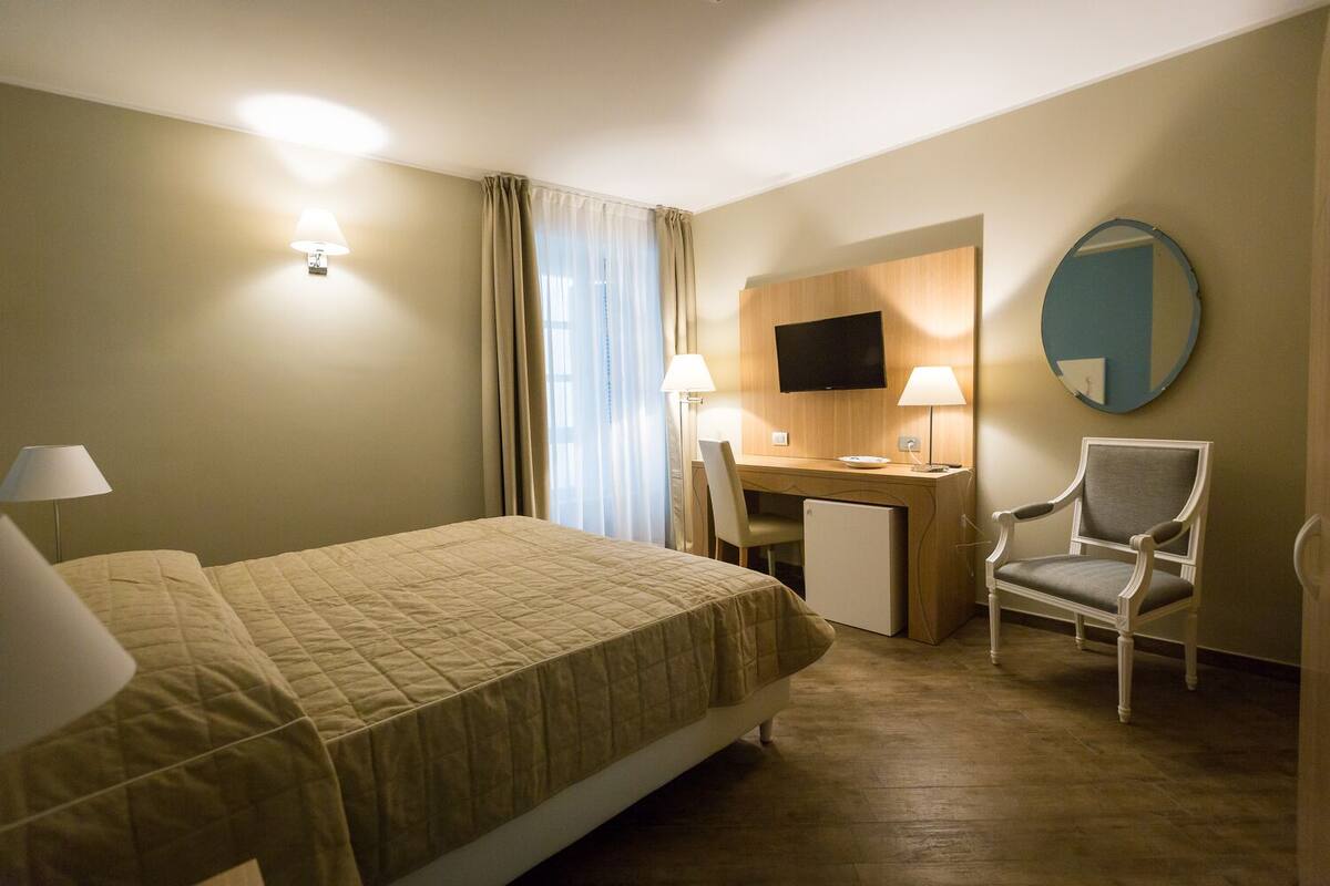 A hotel room with a bed, desk, chair, TV, and a mirror.