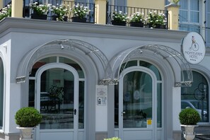 A hotel facade with arched windows, a sign indicating the Monteverde Hotel, and potted plants on the balcony.