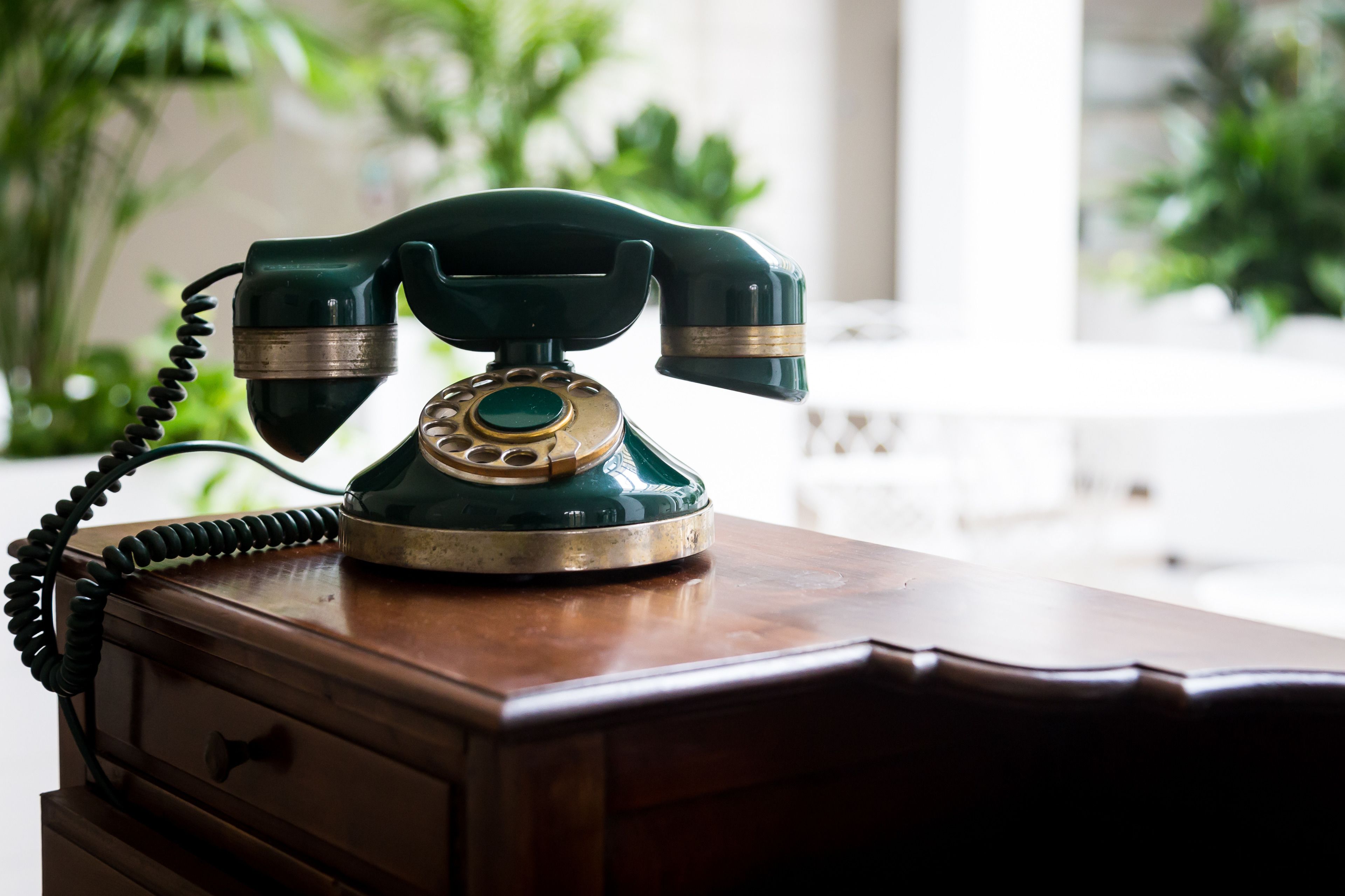 A vintage green rotary dial telephone on a wooden desk.